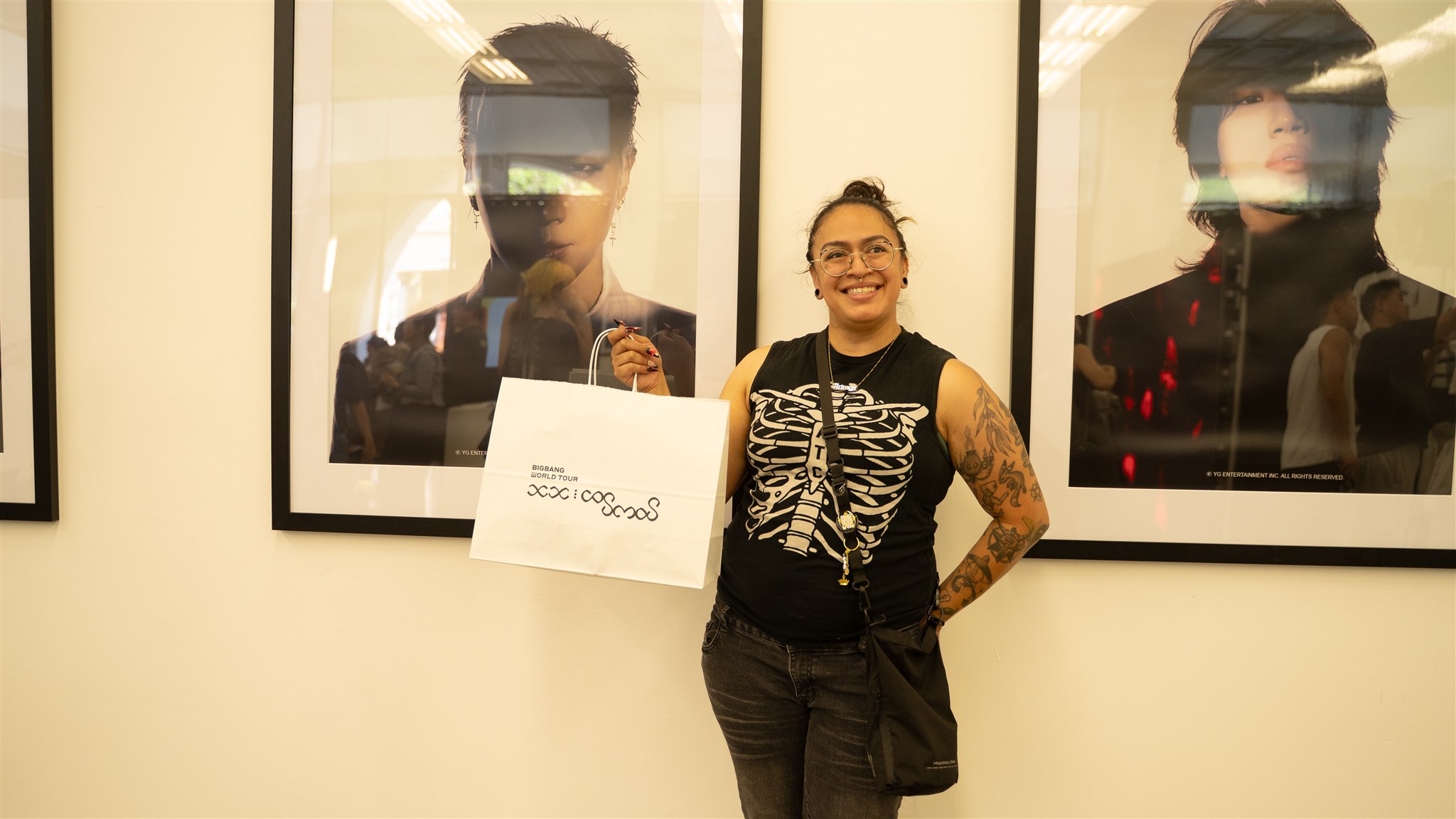 Event attendee holding a BIGBANG shopping bag beside framed portraits
